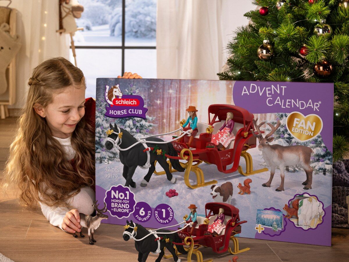Une petite fille joue avec le traîneau, le cheval noir et le renne du grand calendrier de l’Avent Schleich Horse Club, devant un sapin de Noël