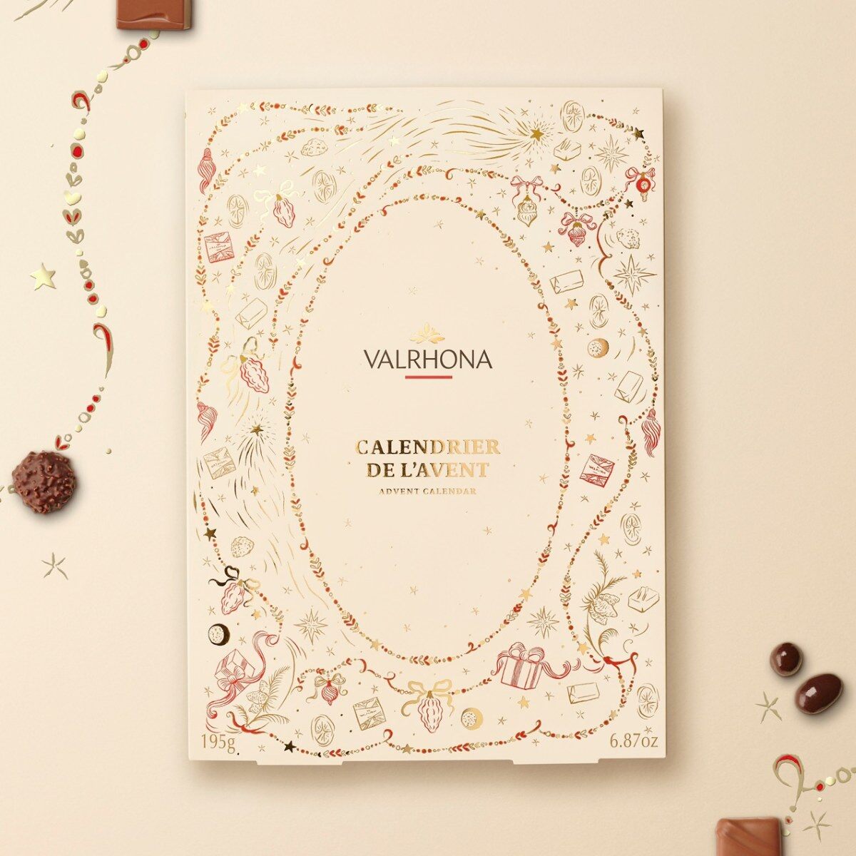 L’écrin du calendrier de l’Avent Valrhona 2026 illustré par Safia Ouares, entouré de chocolats et de guirlandes dorées