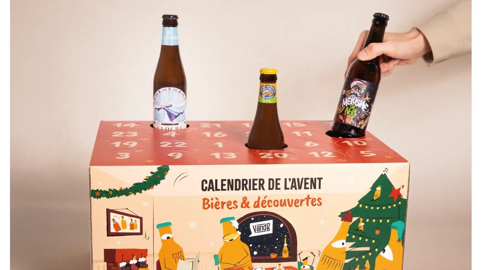 Une main dépose une bouteille de bière dans le calendrier de l’Avent V and B Bières et découvertes 2026