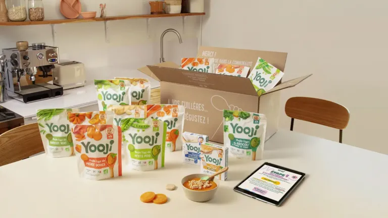 Colis Yooji ouvert et sachets de purées bébé surgelées sur une table de cuisine