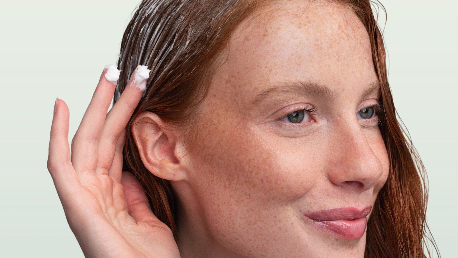 Une femme aux cheveux mouillés applique un soin crème sur ses longueurs, visuel de la marque Yuumae